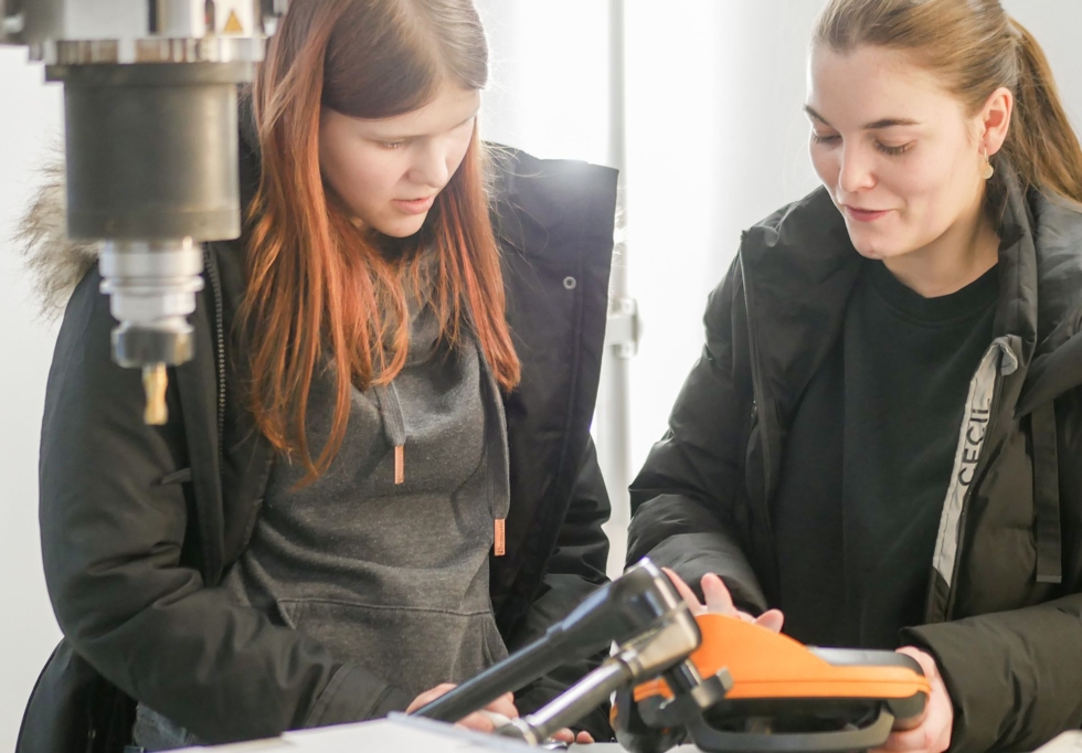 Zwei junge Frauen arbeiten in einer Werkstatt an einer Maschine.